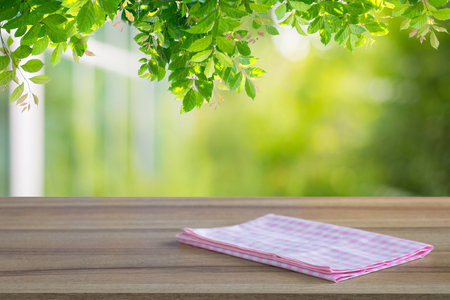 Wooden table and pink checked tablecloth over blurred background nature and green tree leaves and bokeh under the tree background. Can be used for display or montage for show your products.の写真素材