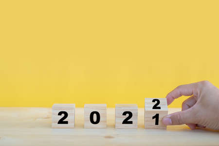 Close up image of hand flipping wooden cubes blocks on yellow background for change year 2021 to 2022. New year and holiday concept.の写真素材