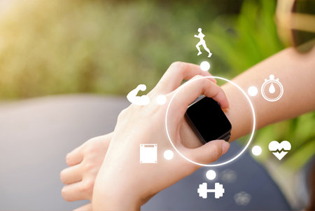 Athlete hands touching screen and using and setting  on smart watch before exercise outdoor in the park. Various exercise-related icons are displayed in the image to illustrate the variety of uses.の写真素材