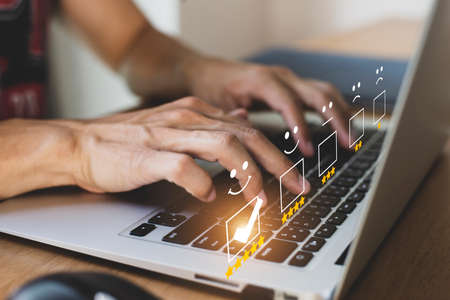 Businessman pressing pressing face emoticon on the laptop on desk and selecting smiley face icon and a 5 star rating. Demonstrates that customer satisfaction is essential to a successful business.の写真素材
