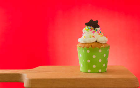 Cupcake against red background on wooden cutting boardの写真素材