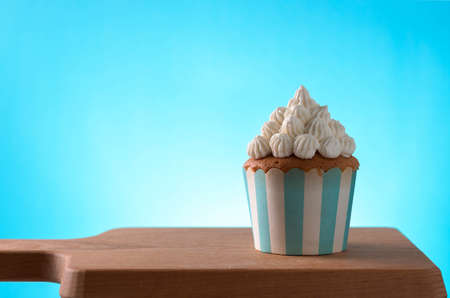 Cupcake against blue background on wooden cutting boardの写真素材