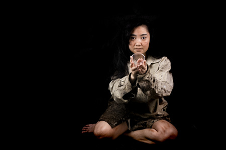 Young and dirty beggar asking hand holding for some money on black backgroundの写真素材