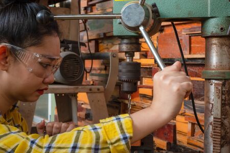 Women standing is craft working drill wood at a work bench with Drill Press power tools at carpenter machine in the workshopの写真素材
