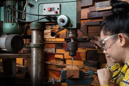 Women standing is craft working drill wood at a workbench with Drill Press power tools at carpenter machine in the workshopの写真素材