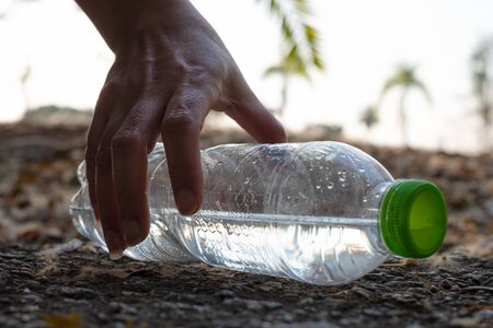 Close up Hand picking up clear plastic bottle water drink with a green cap on the road in the park at blurred background, Trash that is left outside the bin, litter on ground in the garden, Save earth conceptの写真素材