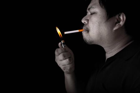The fat man lighting up a joint with lighter smoking at the black background, close up image of cigarette smoke spread in handの写真素材