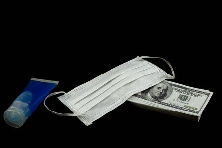 Doctor mask and virus protection alcohol gel bottle and money a stack of 100 US dollars banknote a lot of at the black background, That was It costs expensive price and high priced products conceptの写真素材