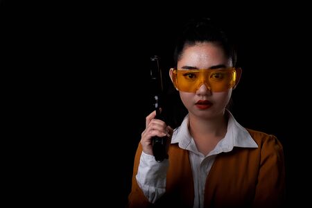 Portrait beautiful asea woman wearing a yellow suit one hand holding a pistol gun at black background, Young sexy girl long hair with a handgun look at the camera, Pretty women stands with a pistolの写真素材