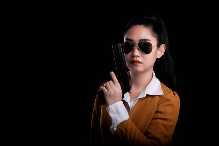 Portrait beautiful asea woman wearing a yellow suit one hand holding a pistol gun at black...