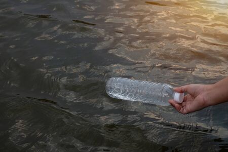 Woman hand to pick up the used waste plastic bottle on the water in a canal