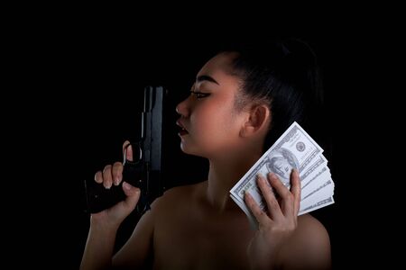 Portrait beautiful Asia woman one hand holding a gun and money banknote 100 DSD at black background, Young sexy girl long hair with a handgun, Pretty women stand with a pistolの写真素材
