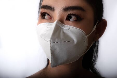Close up of young Asia woman putting on a medical mask to protect from airborne respiratory diseases as the flu covid-19 PM2.5 dust and smog at gray background, Safety virus infection conceptの写真素材