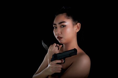 Portrait beautiful Asia woman one hand holding a gun and karambit knife at the black background, Young sexy girl long hair with a handgun, Pretty women stand with a pistol, look at cameraの写真素材