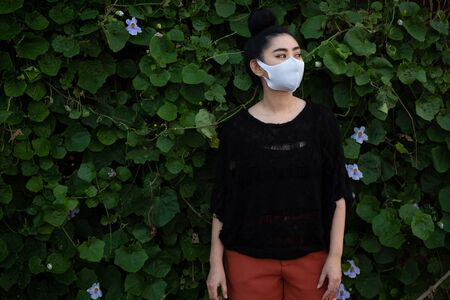 Portrait young Asia woman standing and putting on a fashion mask at leaf wall background with copy...