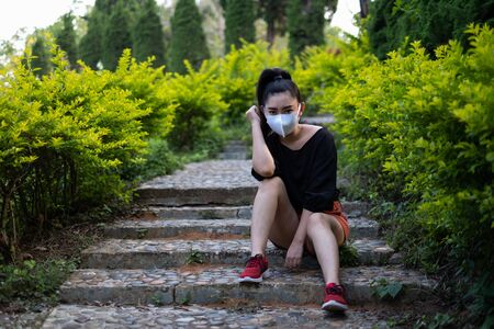 Young Asia woman sit and put on a face mask to protect from airborne respiratory diseases as the flu dust and smog in the park, Women safety virus infection conceptの写真素材