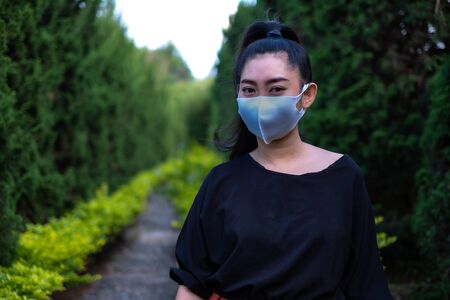 Young Asia woman standing and put on a face mask to protect from airborne respiratory diseases as the flu dust and smog in the park, Women safety virus infection conceptの写真素材