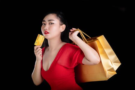 Portrait of a beautiful young Asia woman wearing a red dress holding credit card and shopping bags...