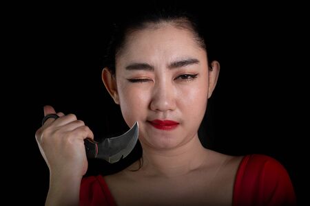 Portrait beautiful Asia woman wearing a rad dress one hand holding Karambit knife at the black background, Young sexy girl long hair with a look at the cameraの写真素材