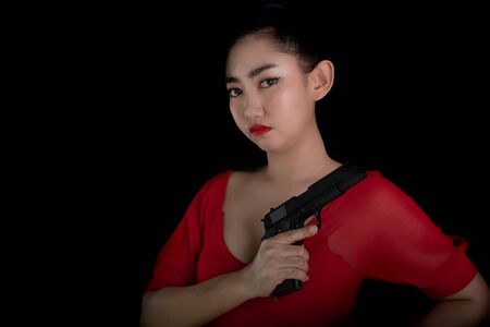 Portrait beautiful Asia woman wearing a rad dress one hand holding pistol gun 11mm. at the black background, Young sexy girl long hair with a handgun look at the camera, Pretty women stand with a gunsの写真素材