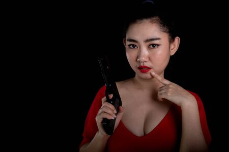 Portrait beautiful Asia woman wearing a rad dress one hand holding pistol gun 11mm. at the black background, Young sexy girl long hair with a handgun look at the camera, Pretty women stand with a gunsの写真素材