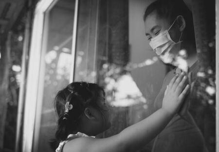 Mother wear face mask meeting daughter and touching hand through the window because of the quarantine Corona Virus Covid-19, social distancing, Black and white pictureの写真素材