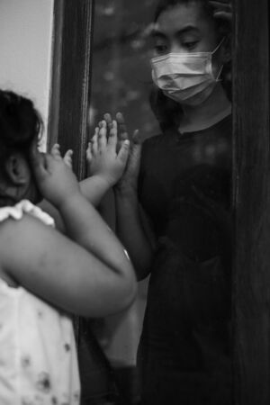Mother wear face mask meeting daughter and touching hand through the window because of the quarantine Corona Virus Covid-19, social distancing, Black and white pictureの写真素材