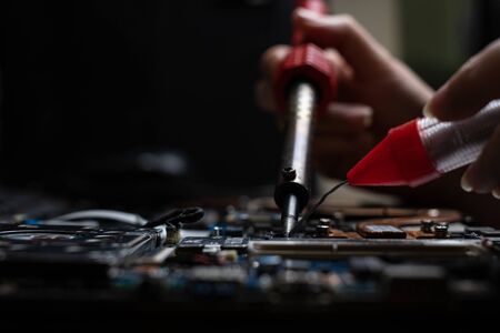 Close-up hand technician repairing broken laptop notebook computer with electric soldering Ironの写真素材