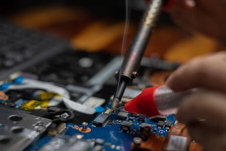 Close-up hand technician repairing broken laptop notebook computer with electric soldering Iron