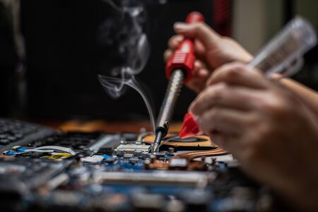 Close-up hand technician repairing broken laptop notebook computer with electric soldering Ironの写真素材