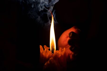 Hand protecting candle light from the wind in darkness on black backgroundの写真素材