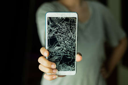 The woman standing and holding smartphone screen is cracked on black background