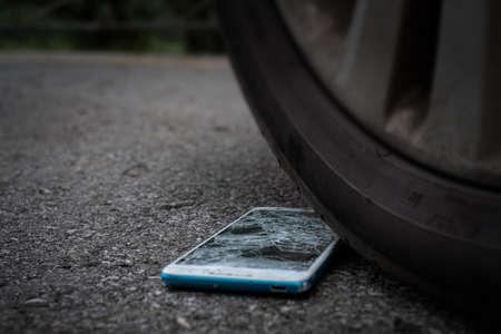 Smartphone screen is cracked flat on the road from moving a car tire at the front and back...