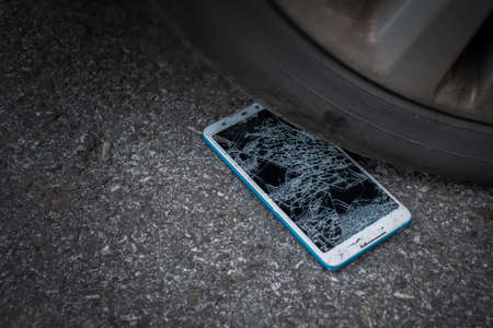 Smartphone screen is cracked flat on the road from moving a car tire at the front and back background is blurredの写真素材