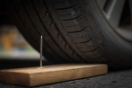 Close up a metal nail on board wood nearly to puncture into wheel tireの写真素材