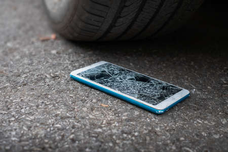 Smartphone screen is cracked flat on the road from moving a car tire at the front and back background is blurredの写真素材