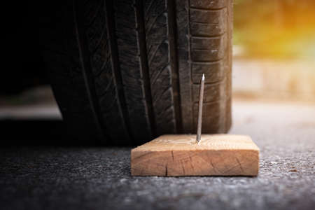 Close up a metal nail on board wood nearly to puncture into wheel tireの写真素材