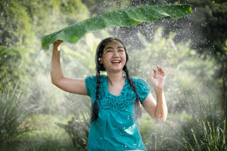 Portrait of a young Asia woman with black hair holding a banana leaf in the raining at the green garden backgroundの写真素材