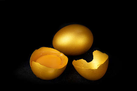 Golden eggs and half broken egg with yolk isolated at the black background