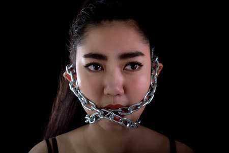 Portrait young Asia woman covered mouth by a steel chain and lock to forbidden him the free...