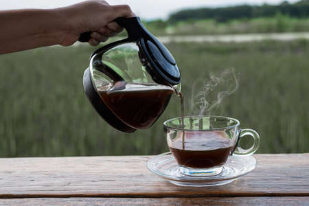Woman handhold a coffee pot and drop to the glass on the wood table at blurred background