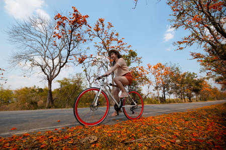 Young woman happy enjoying the outdoor leisure activity riding a bike and smiling for happiness the healthy lifestyles at full of beautiful orange flower background, The concept of travel and freedomの写真素材