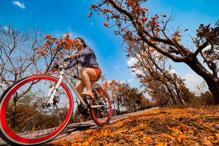 Young woman happy enjoying the outdoor leisure activity riding a bike and smiling for happiness the healthy lifestyles at full of beautiful orange flower background, The concept of travel and freedomの写真素材