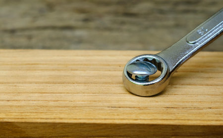 Close-up wrench screwing nut a furniture screw into a wooden plank, The effort  wrong of tools as a...