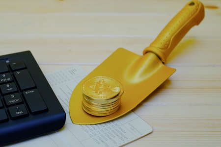Close up of gold bitcoin coins on bank passbook with a golden shovel on wooden table