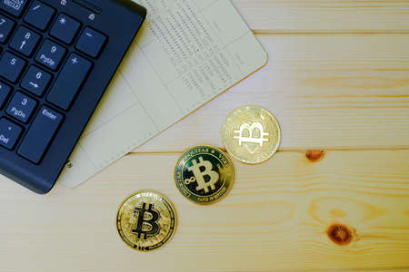 Close up of gold Bitcoin coins on bank passbook with laptop keyboard on wooden table