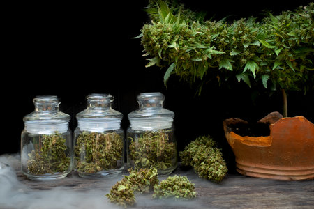 The marijuana buds in a clear glass jar sit on a smoky floor at the black backgroundの写真素材