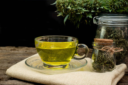 Cannabis tea in a clear glass cup with a marijuana bud in a jar on a wooden and the black backgroundの写真素材