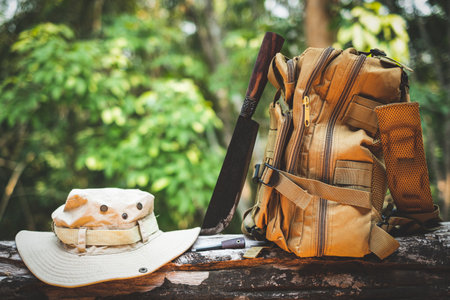 Equipment for survival bucket hat backpack hiking knife camping flashlight resting on wooden timber in the background is a forestの写真素材