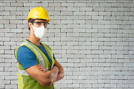 Engeener in helmet wearing medical mask for protect virus on brick wall white background, copy space for text.の写真素材